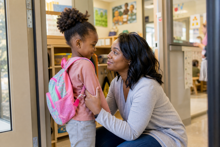 Black mother hugging preschool child goodbye near a classroom doorway