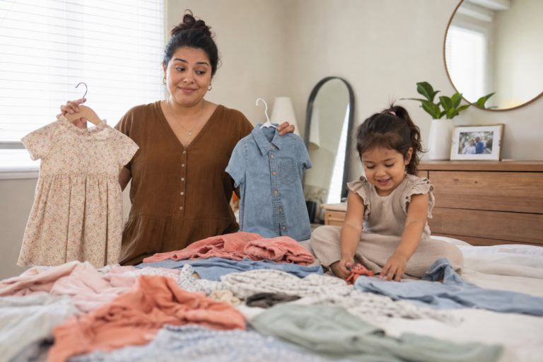 Latina mother choosing children’s outfits for family photos while a preschool child plays nearby