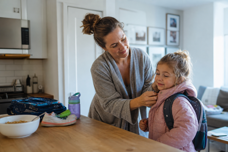 White mother helping preschool child with a jacket during a busy morning at home