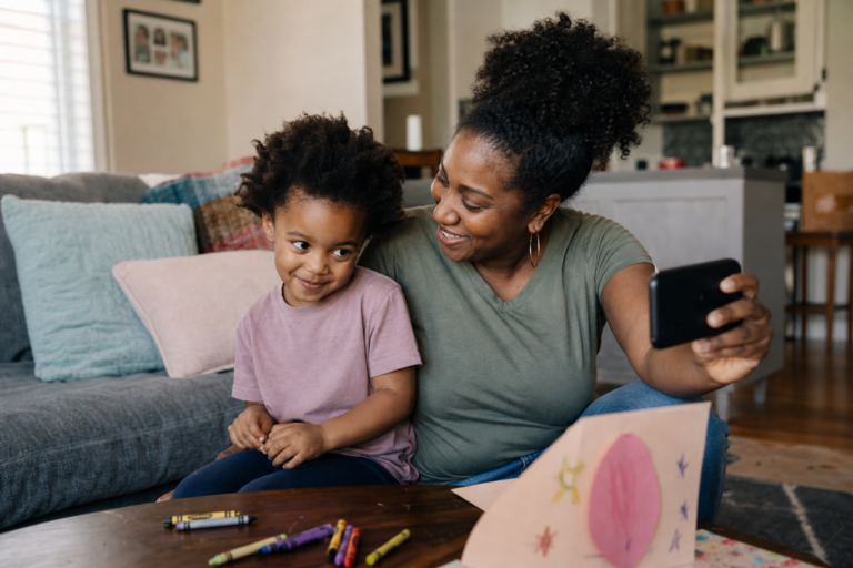 Black mother helping her young child record a birthday message video in a living room