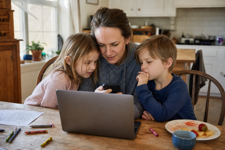 White mother and two young children looking through family video clips at a kitchen table