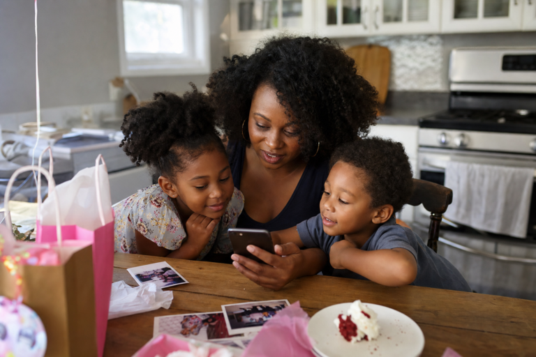 Black mother and two young children looking at family party photos and videos at a kitchen table