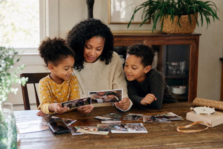 Black mother and two young children looking through family photos at a kitchen table