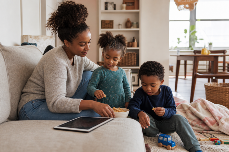 Black mother and two young children relaxing in a living room with an idle tablet nearby