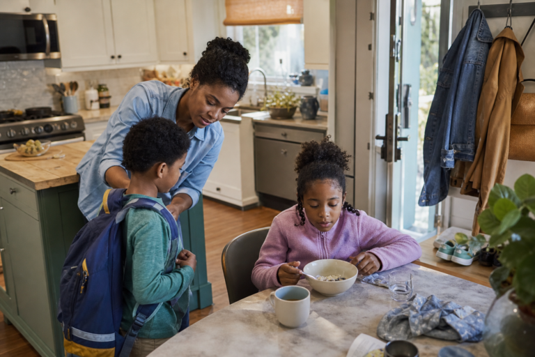 Black mother helping two young children get ready near coats and backpacks in a family kitchen