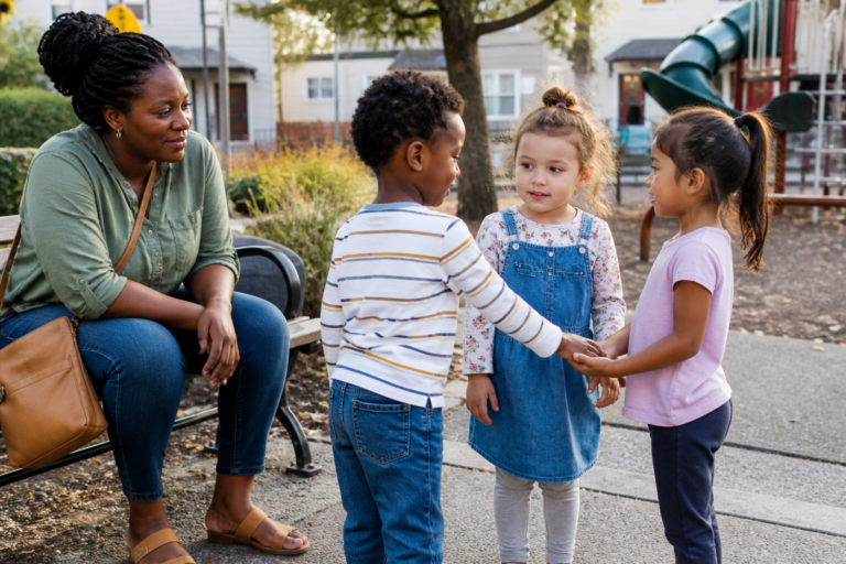 Black mother watching young children navigate a playground friendship moment
