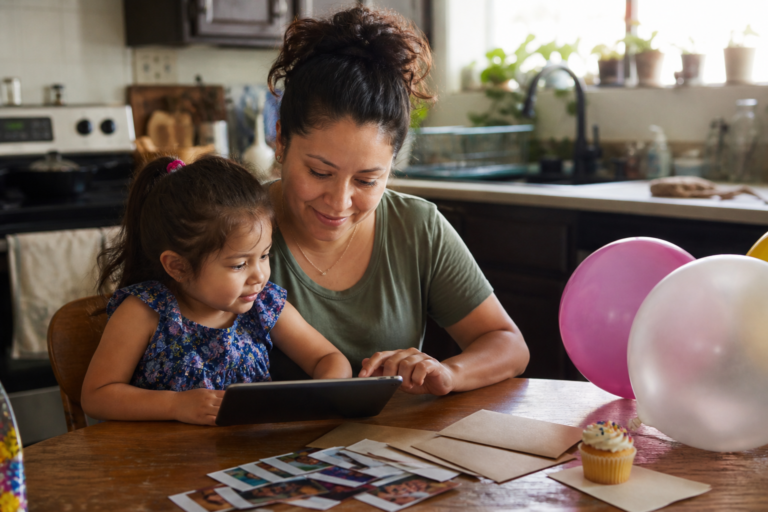 Latina mother and young child looking at family photos for a party invitation video at a kitchen table