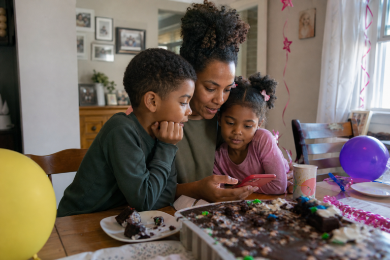 Black mother and two young children watching birthday video clips together after a home birthday party
